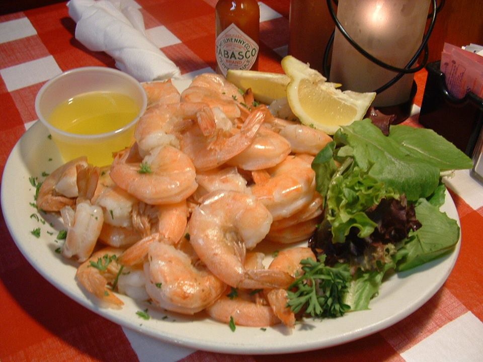 Plate filled with large steamed shrimp served hot with drawn butter garnished with mixed greens