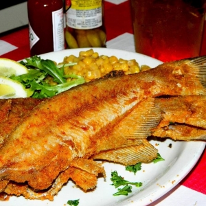 A plate of fried whole catfish with lemons and corn