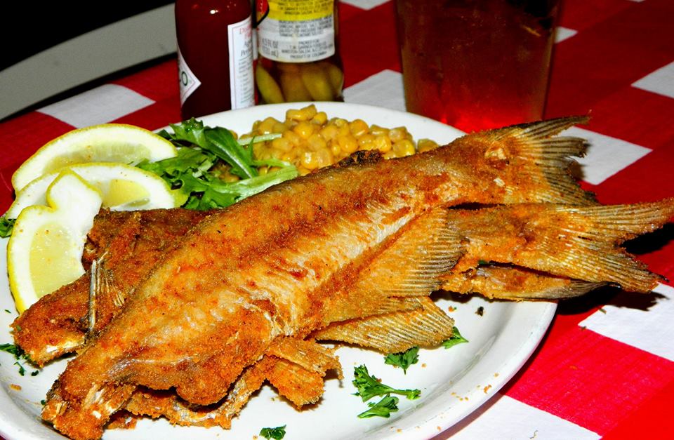 A plate of fried whole catfish with lemons and corn