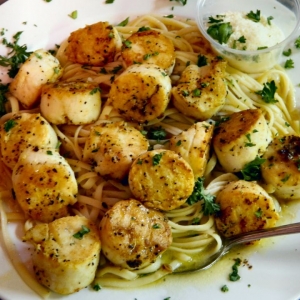 Grilled sea scallops over pasta with a lemon butter sauce garnished with chopped parsley