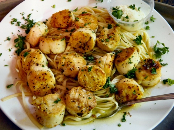 Grilled sea scallops over pasta with a lemon butter sauce garnished with chopped parsley